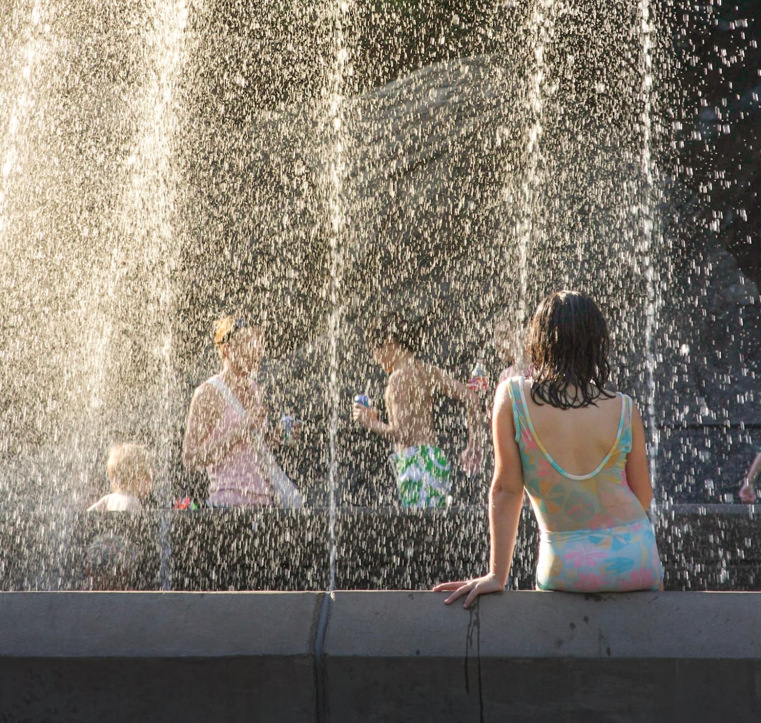 A woman sitting before a fountain as sunlight catches the falling water