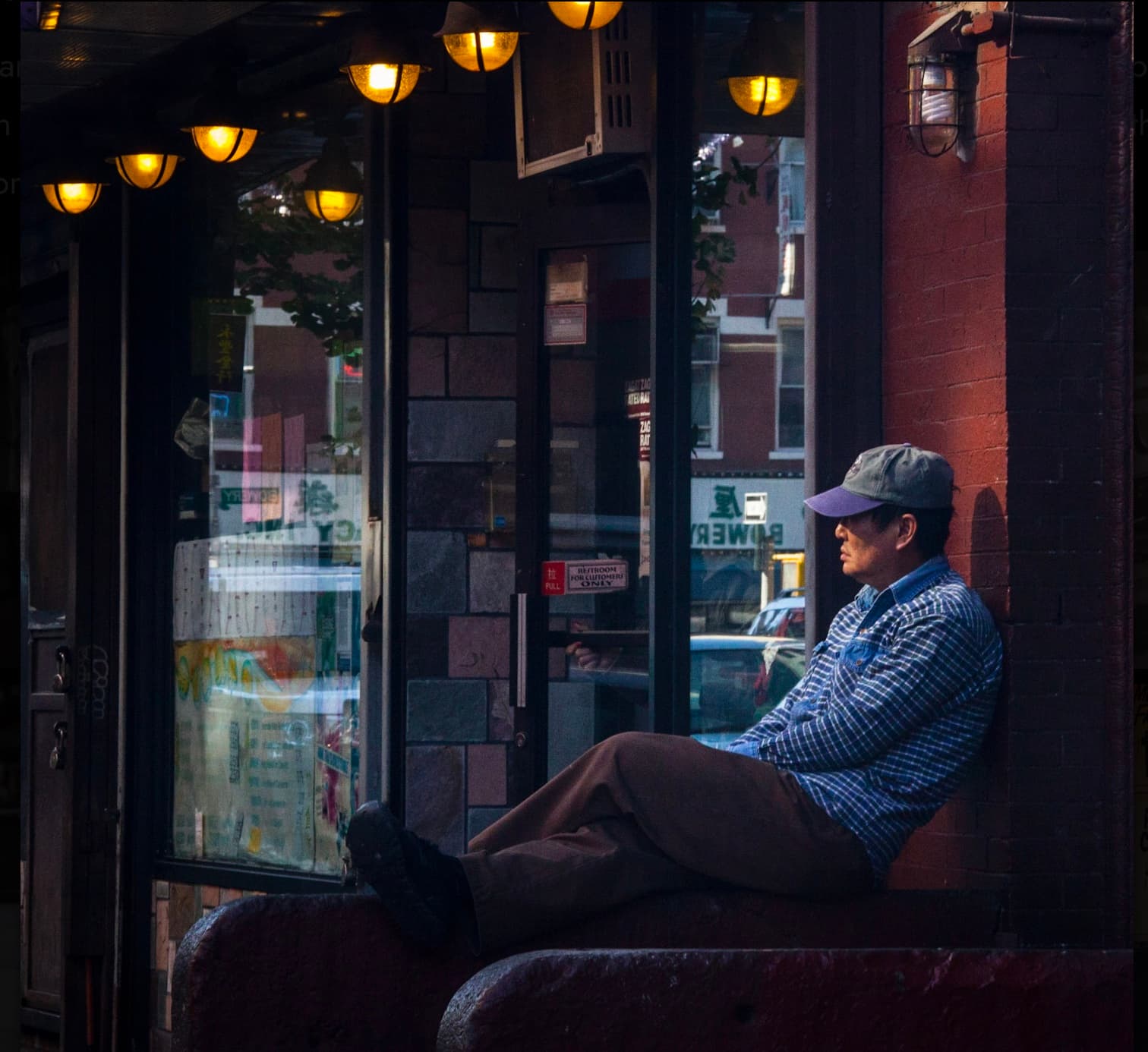 A man sitting quietly beneath a row of glowing lights in a New York storefront